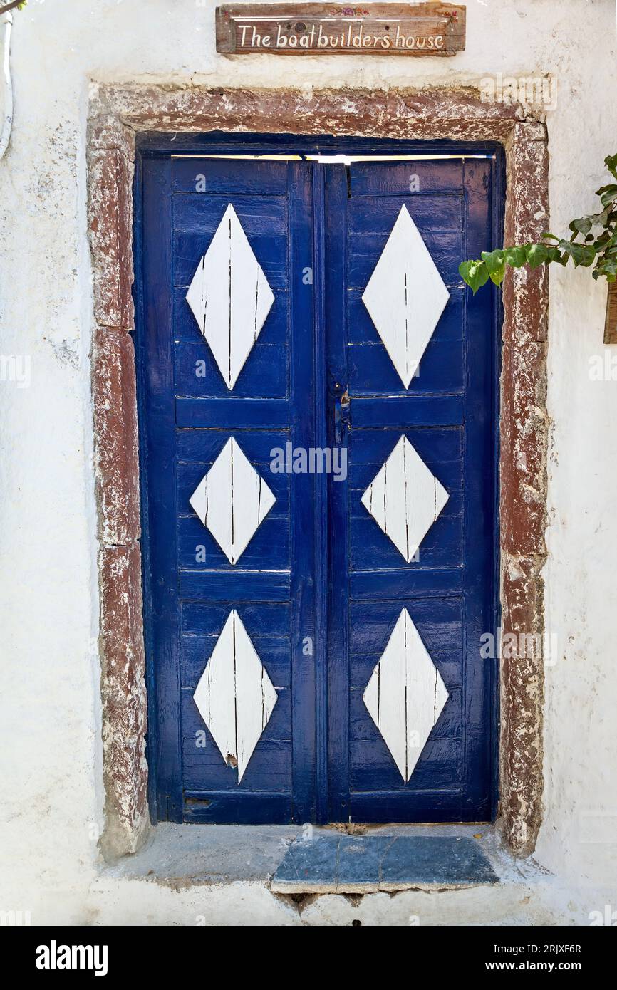 Beautiful wooden blue door, decorated with large diamond shaped white parts. Above the door, the sign says 'The Boat Builder's House'. Stock Photo