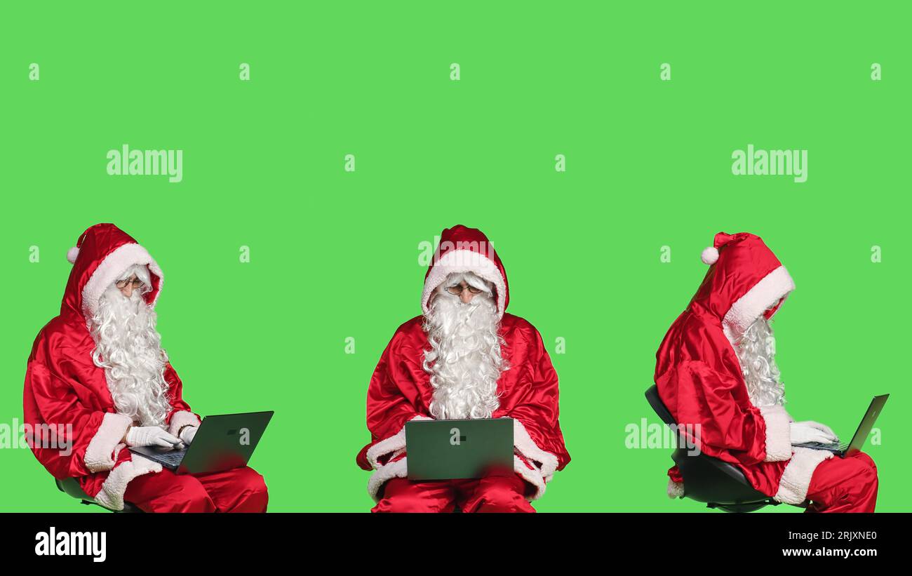 Modern santa claus works on laptop, greenscreen backdrop in studio 