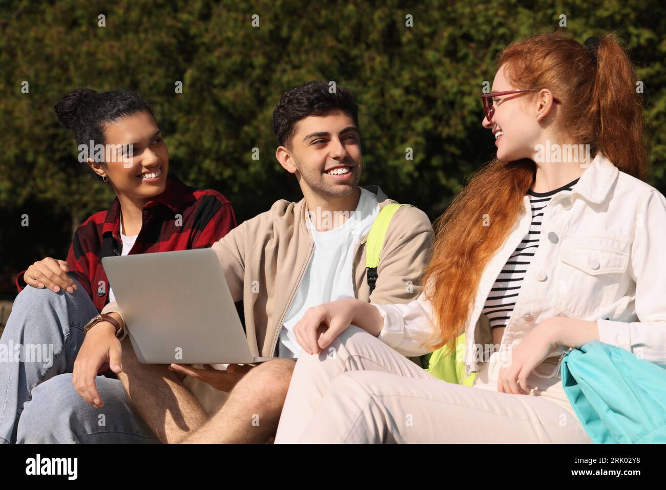 Happy young students studying with laptop together in park Stock Photo ...