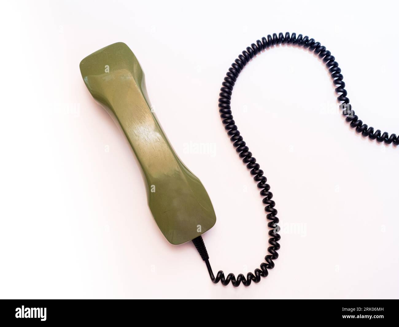 The handset of an old rotary phone lies on a white background. The black spiral cable winds in the picture. Stock Photo