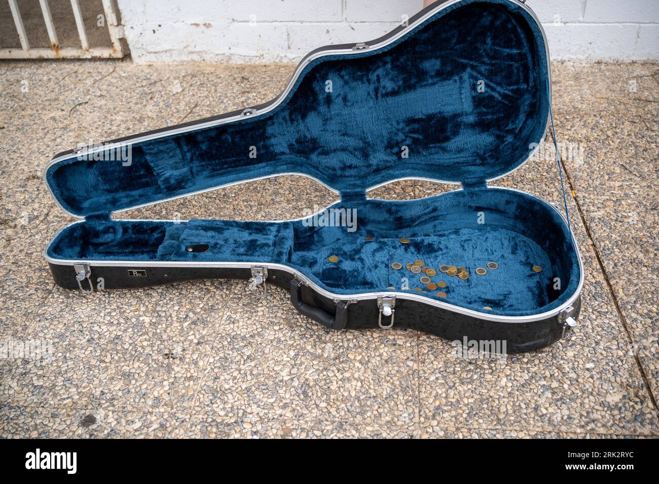 Empty guitar case placed on floor near wall with fence Stock Photo