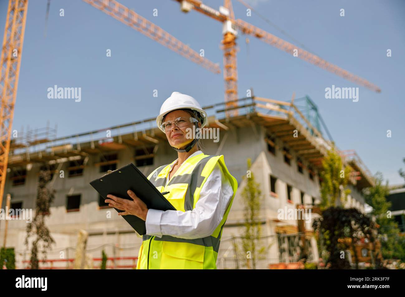 Smiling female construction worker in protective helmet standing against on construction background  Stock Photo