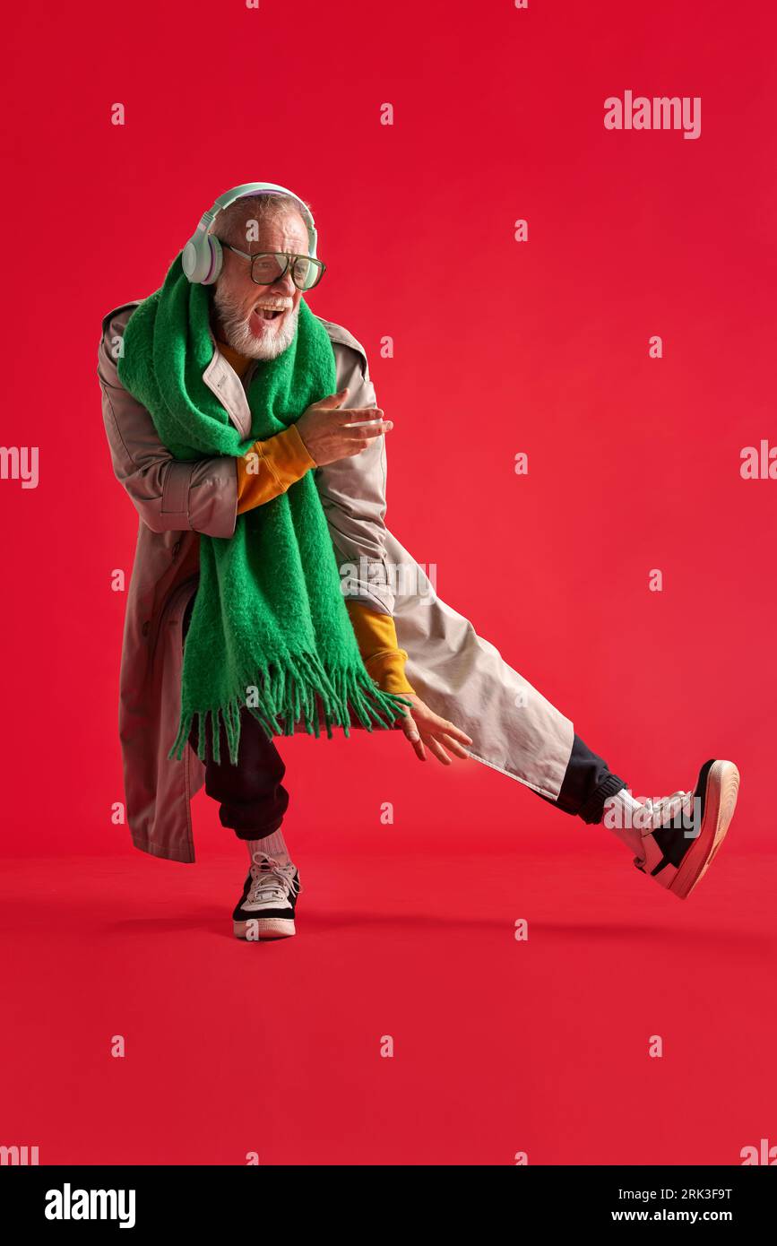 full-length portrait of positive, funny man with beard in bright , casual outfit with headphones who is dancing and singing. Stock Photo