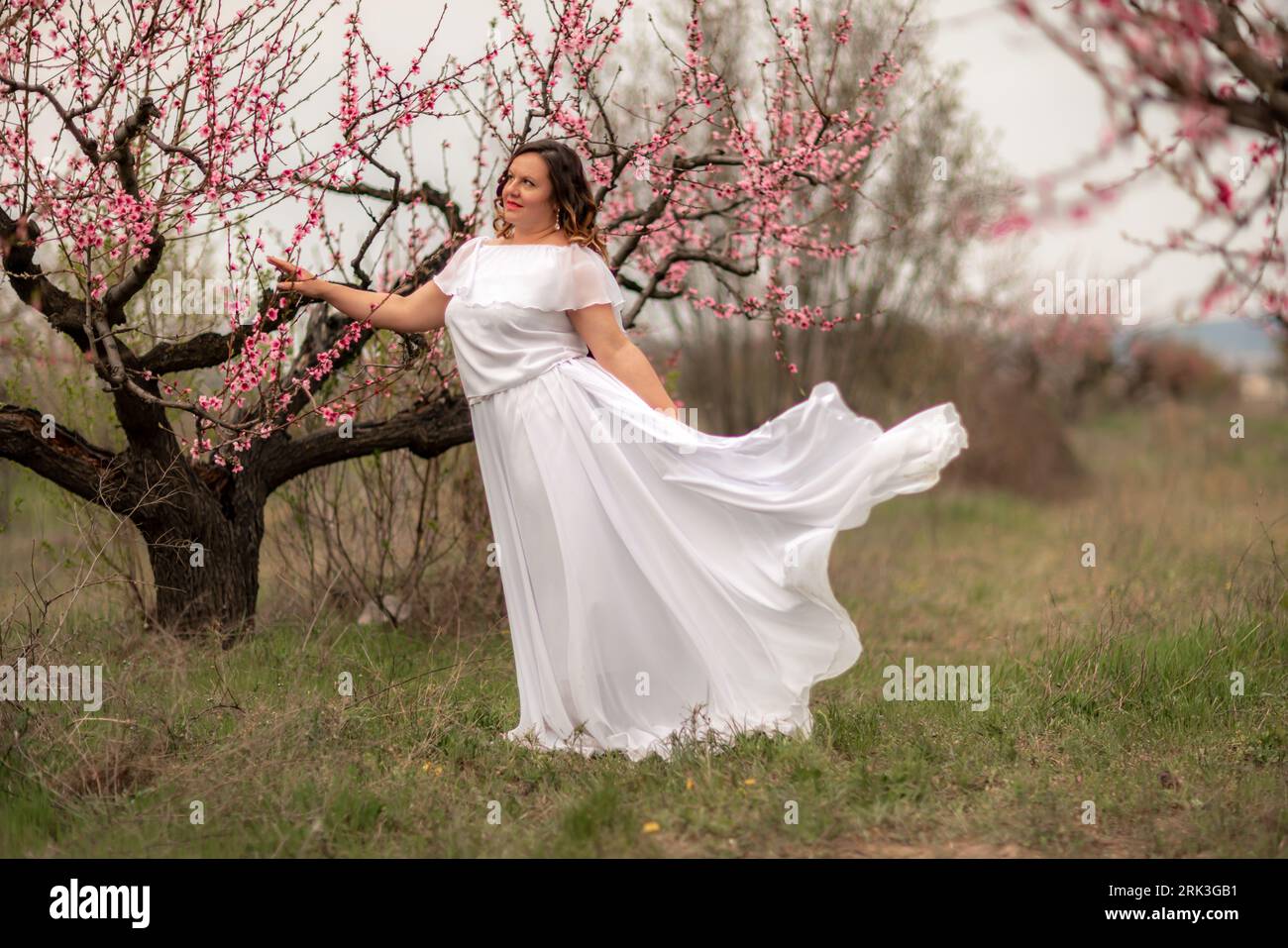 Woman peach blossom. Happy woman in white dress walking in the garden of blossoming peach trees in spring Stock Photo