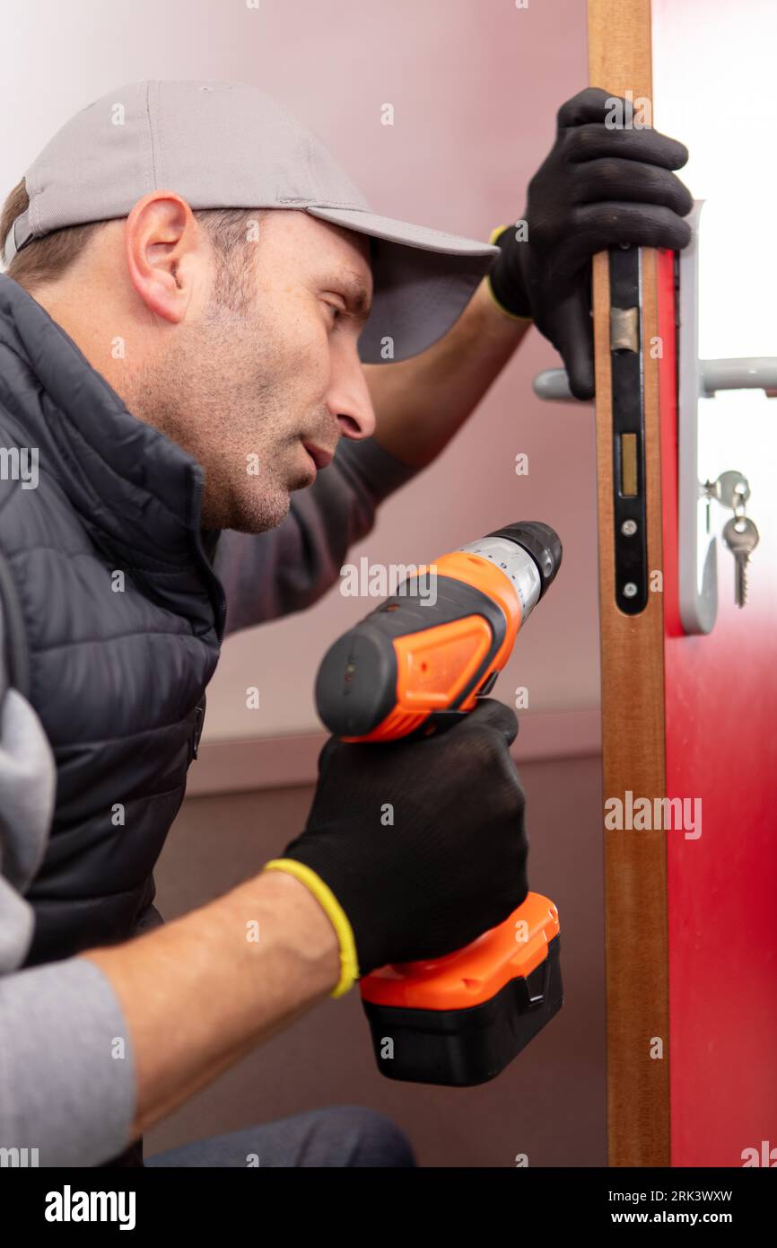 young contractor using cordless drill on door lock Stock Photo