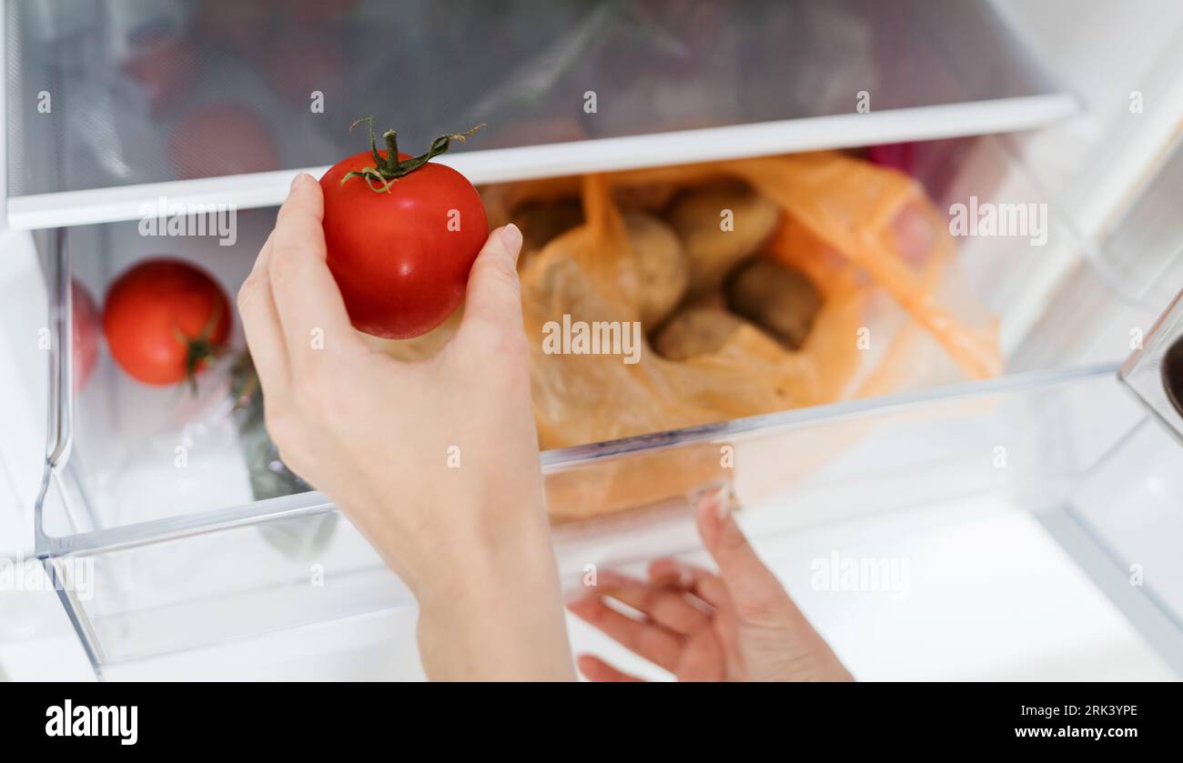 female hand picks up tomato from the refrigerator shelf. healthy food. healthy lifestyle concept Stock Photo