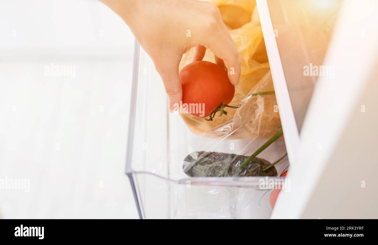 hand picks up tomato from the refrigerator shelf. healthy food. Stock Photo