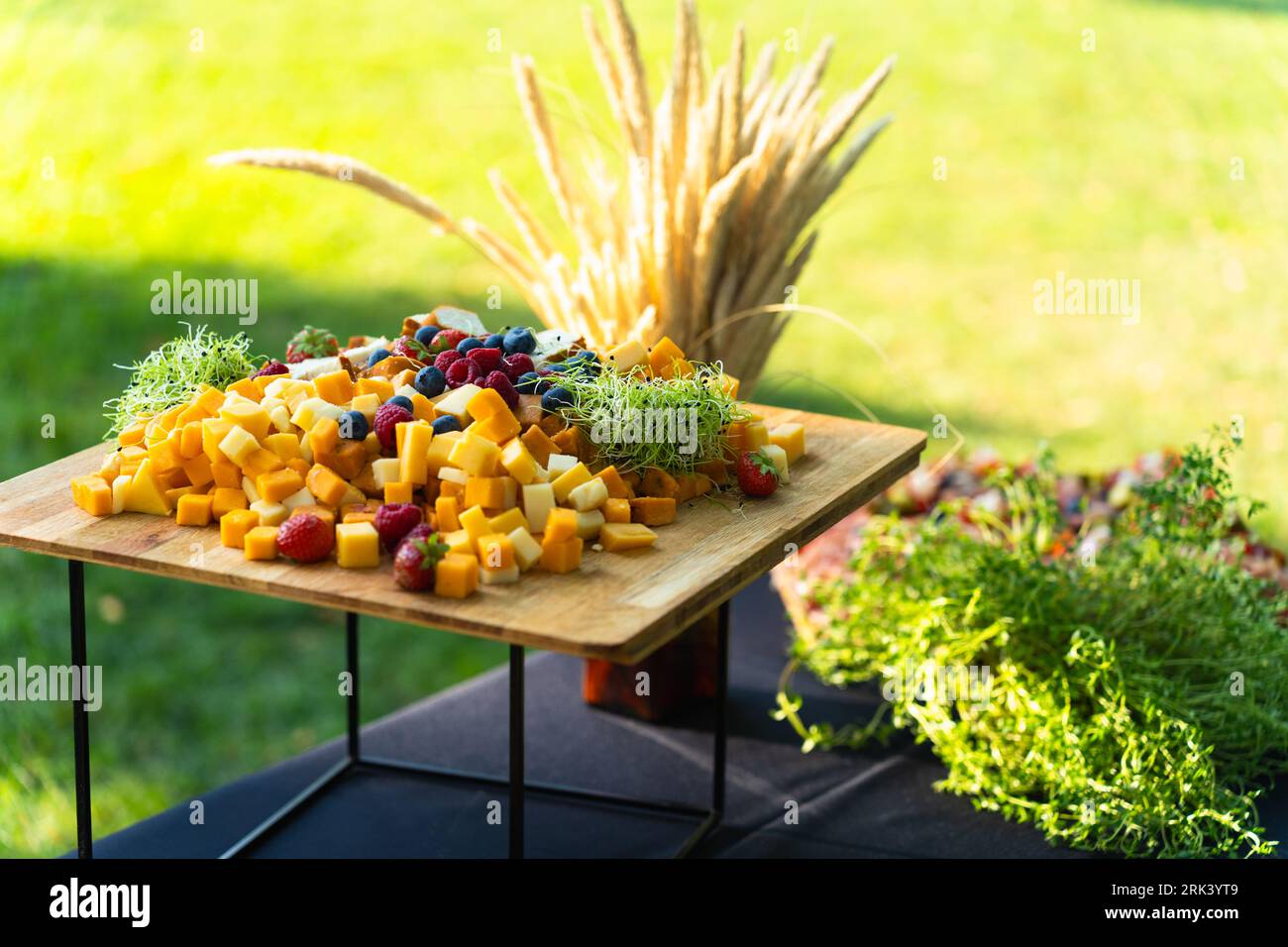 Board with various cheeses and berries cut into cubes for a festive buffet in the yard in the summer Stock Photo