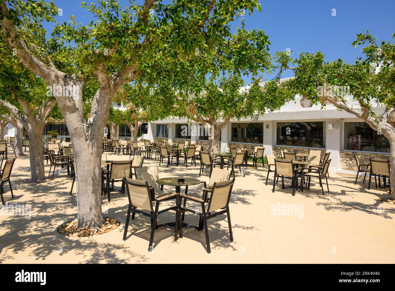 Kos, Greece - May 7, 2023: Cozy Greek hotel cafe terrace with tables and chairs under the trees. Kos Island, Greece Stock Photo