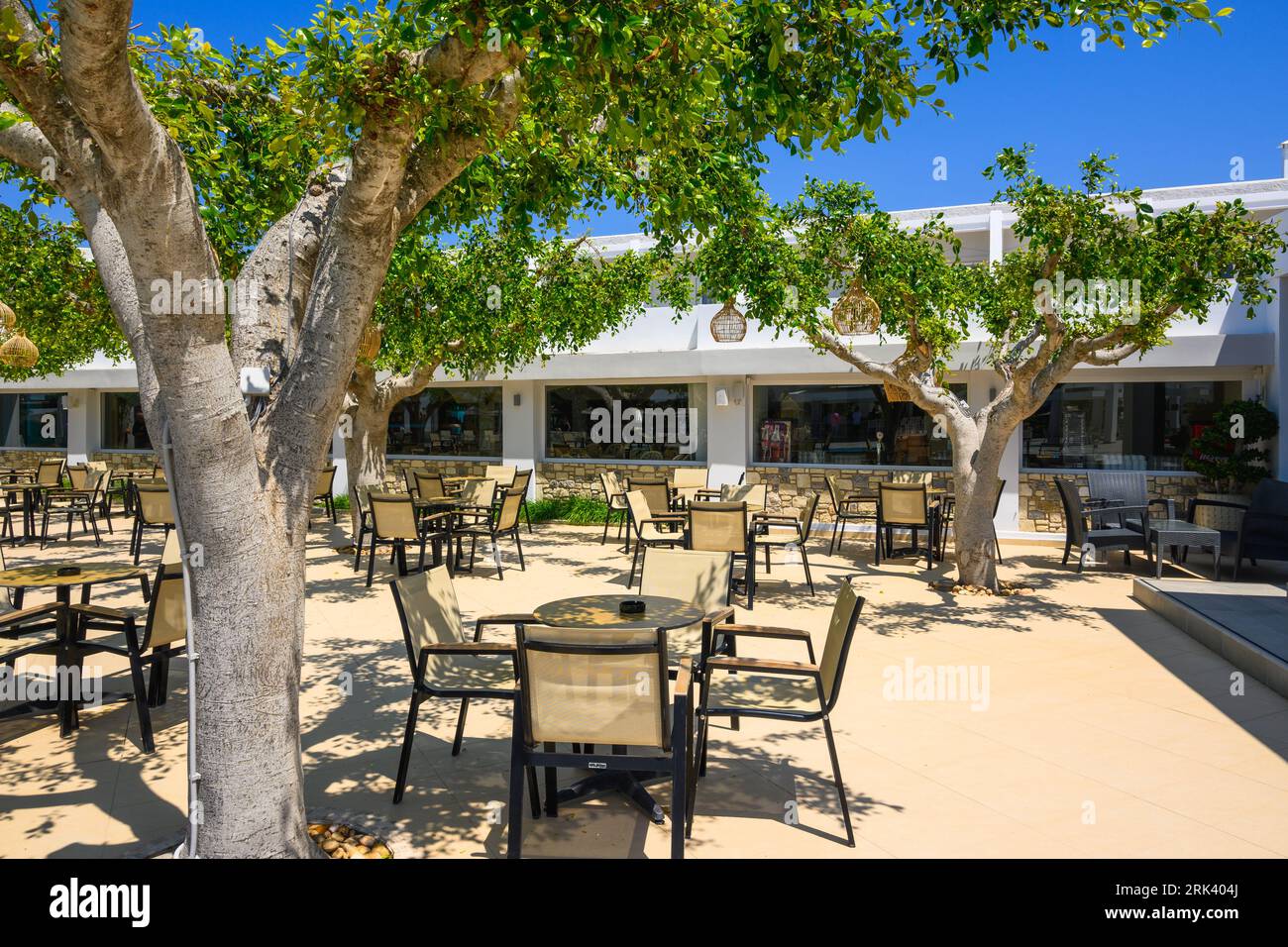 Kos, Greece - May 7, 2023: Cozy Greek hotel cafe terrace with tables and chairs under the trees. Kos Island, Greece Stock Photo
