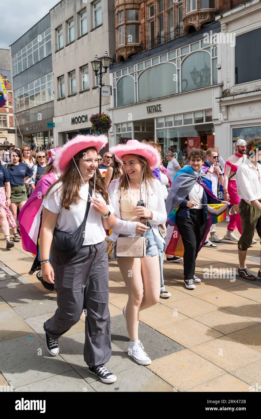 Two young women wearing pink  cowgirl hats walking in Lincoln Pride Parade, High Street, Lincoln City, Lincolnshire, England, UK Stock Photo