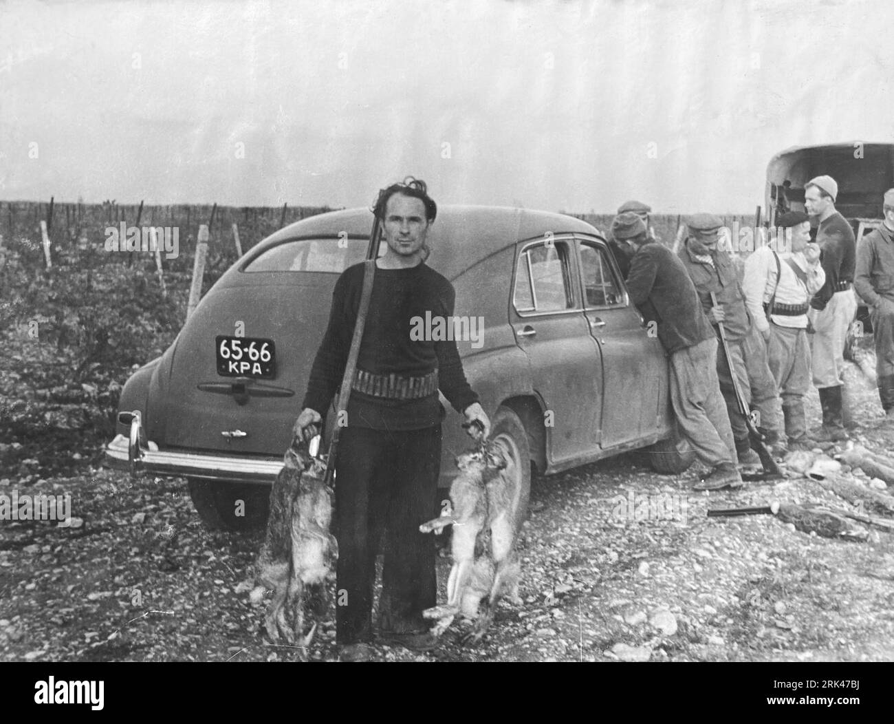 Crimea, USSR - circa 1960: hunter holds dead hares with gun over his shoulder Stock Photo