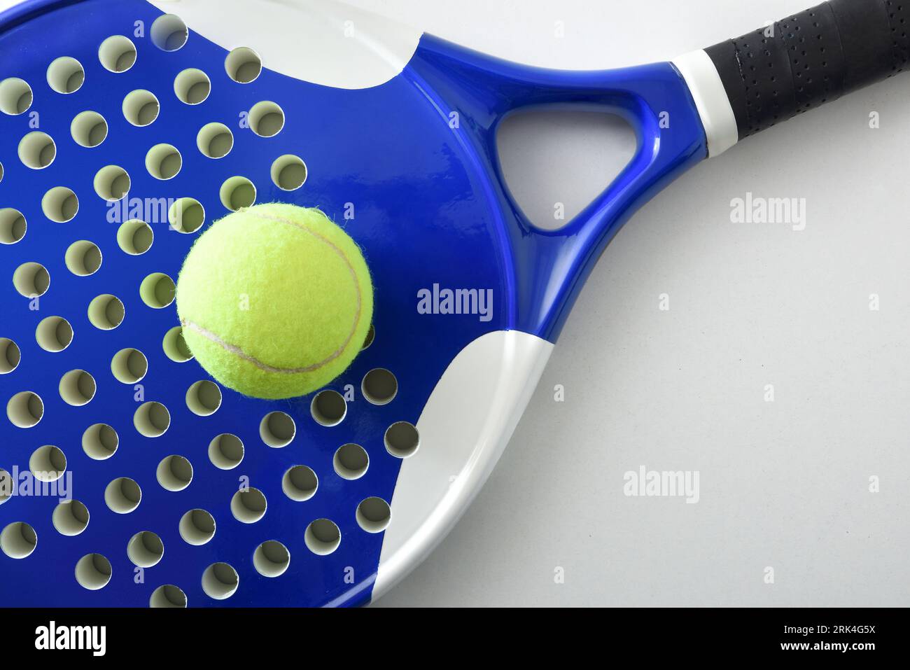 Detail of black and white paddle tennis racket and ball on a white table. Top view. Stock Photo