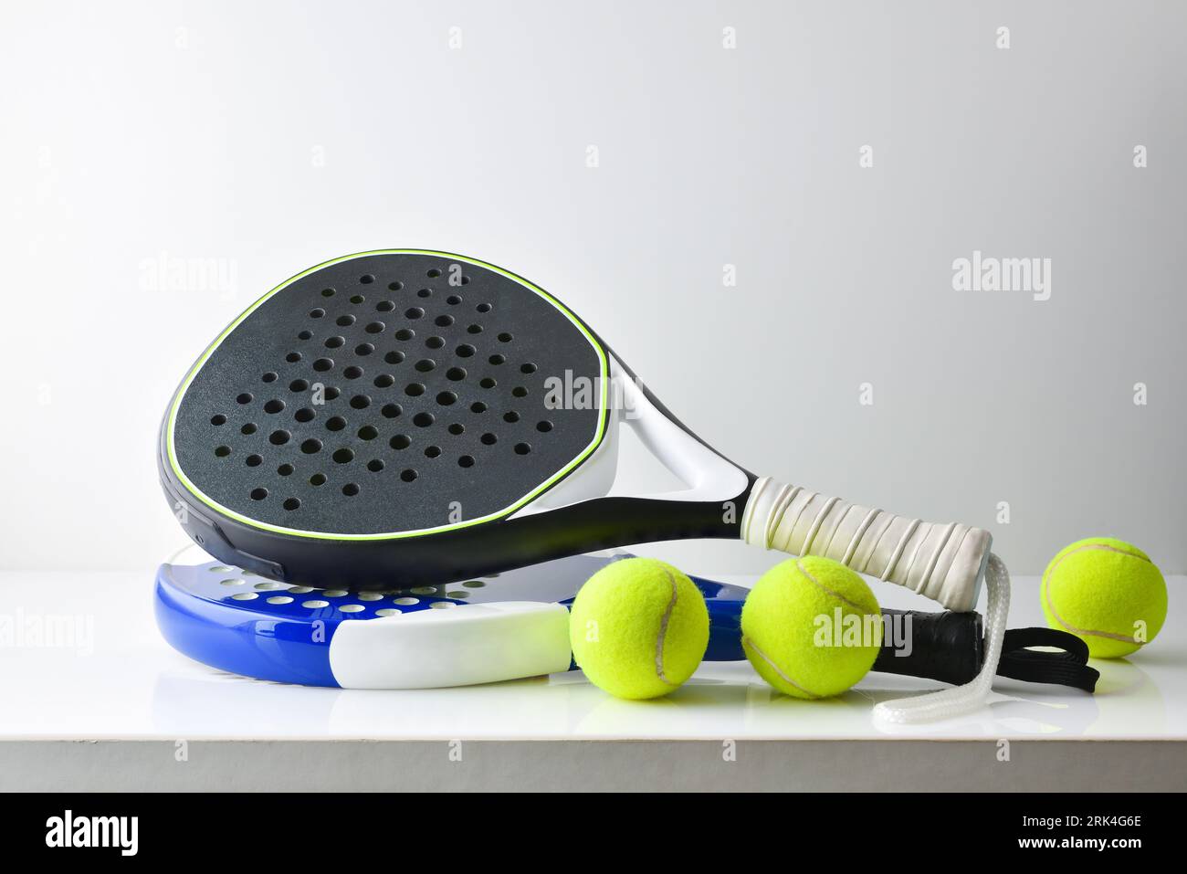 two blue and black paddle rackets on white table with balls and white isolated background. Front view. Stock Photo