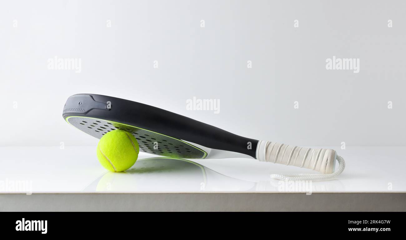 Two black and white paddle tennis rackets resting on a ball reflected on a white table and a white isolated background. Front view. Stock Photo