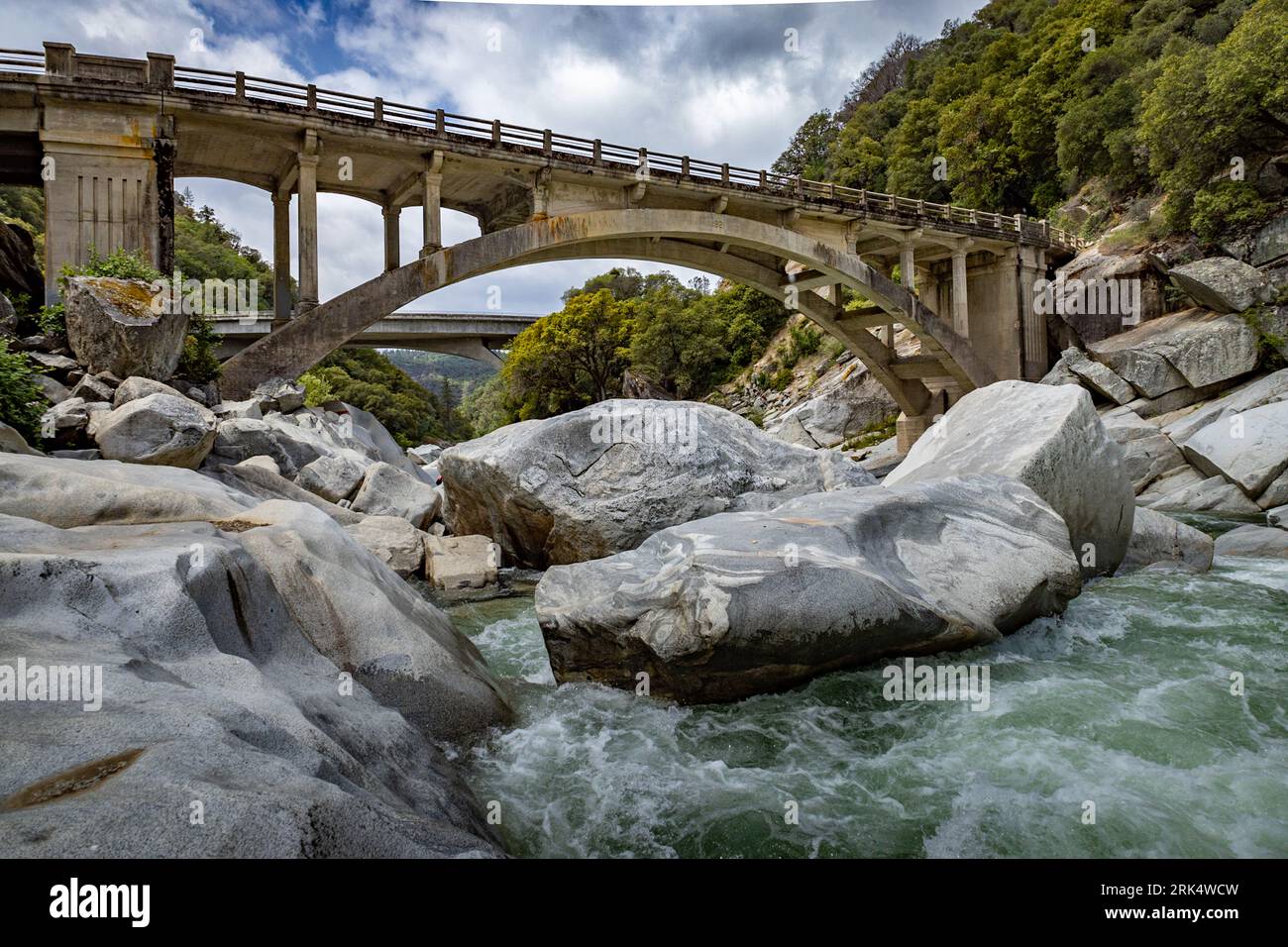 A scenic river seen flowing under a bridge with large rocks in the ...