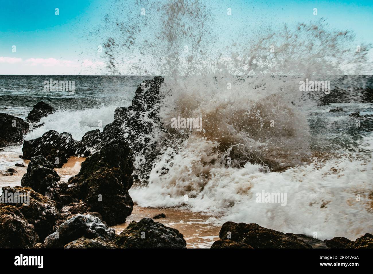 A majestic wave crashing onto the rocky shoreline of a beach ...