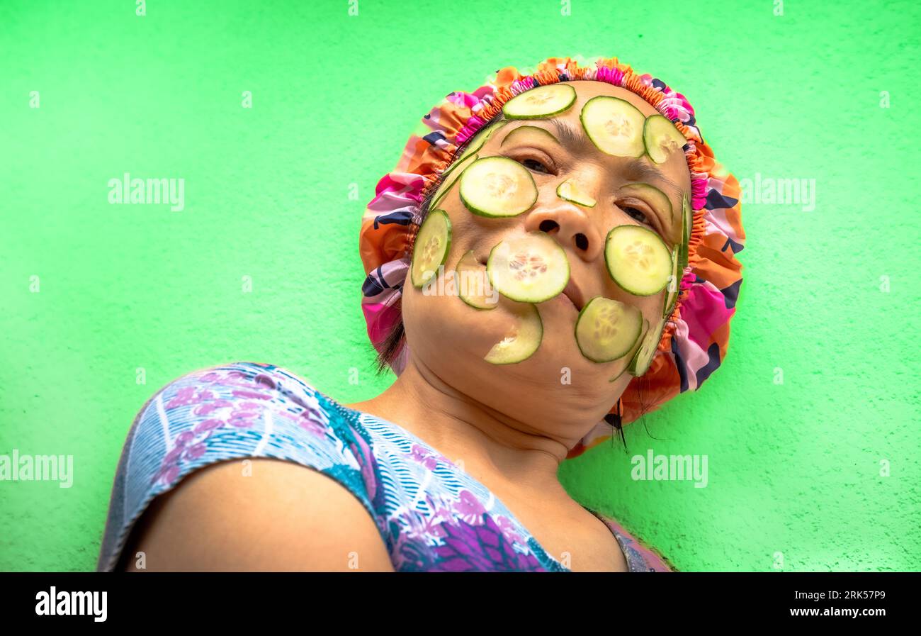 A head and shoulders side on view of a Vietnamese Asian woman with cucumber beauty treatment on her face and wearing a shower cap. Stock Photo