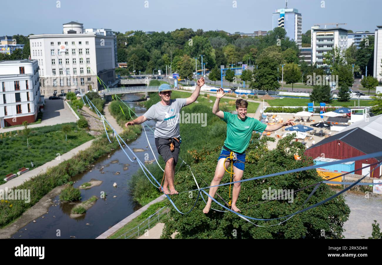Saxony, Chemnitz, Germany. 24 August 2023. Jens Decke (l) and Ruben Langer cross the Chemnitz River in the city center on a highline. The 200-meter long highline course from the Weltecho cultural center to the Deutsche Bank building sets the mood for the Chemnitz Slackfestival. At a height of 17 meters, the professionals balance over the course in the city center. Credit: dpa/Alamy Live News Stock Photo