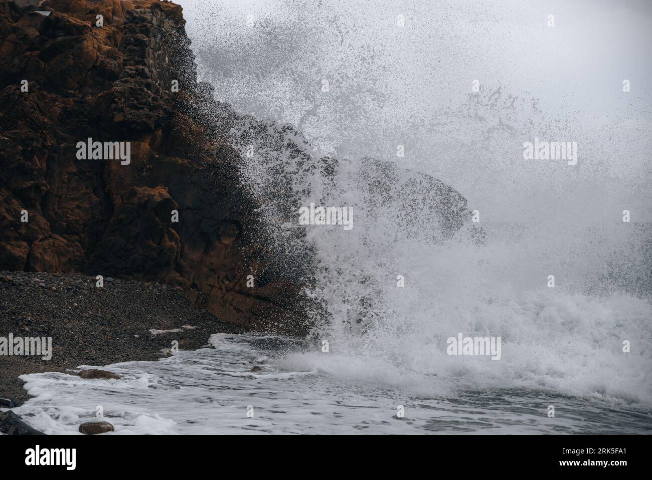 A large wave in the ocean crashing onto the shoreline, creating a white ...