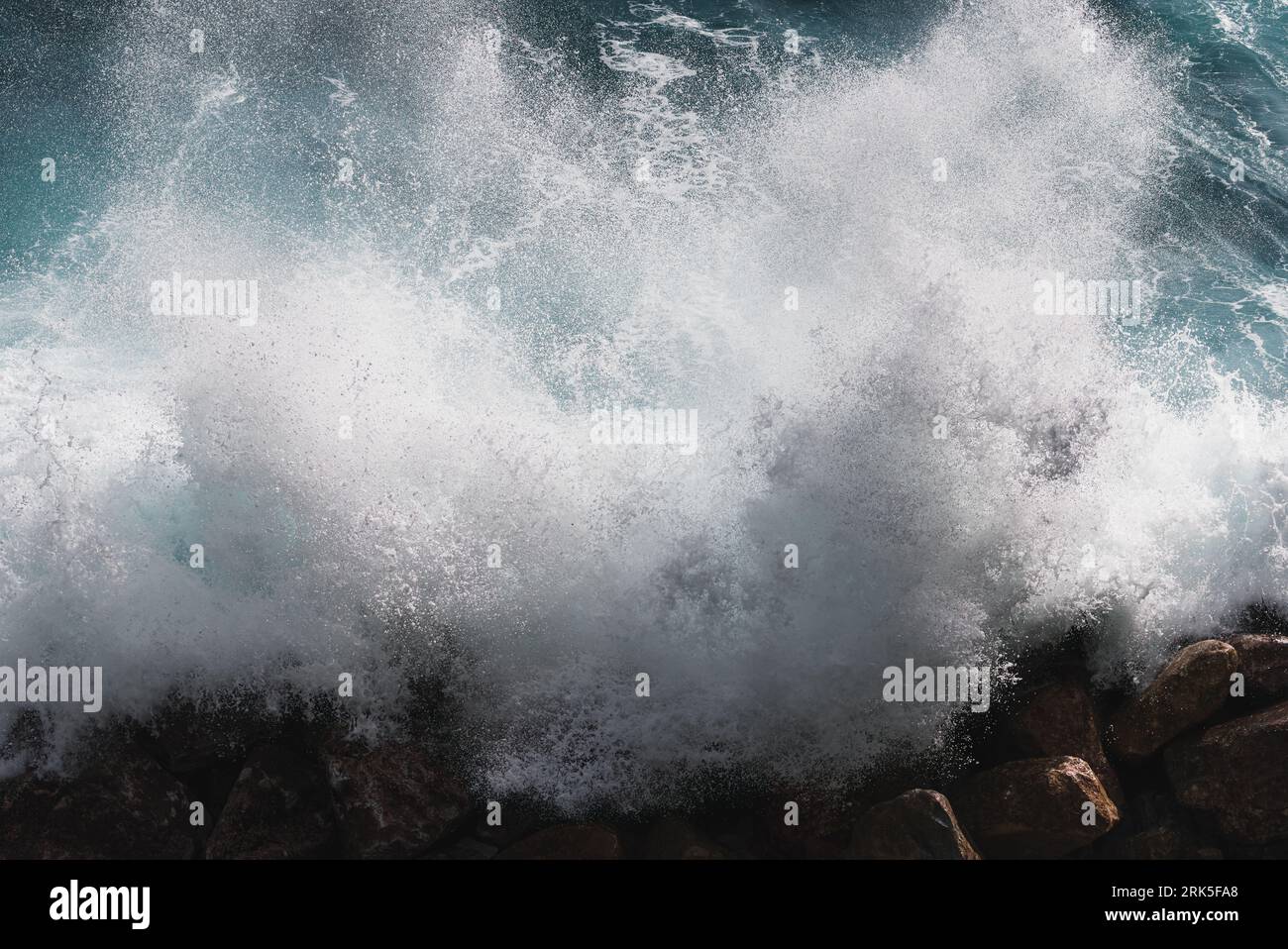A large wave in the ocean crashing onto the shoreline, creating a white ...