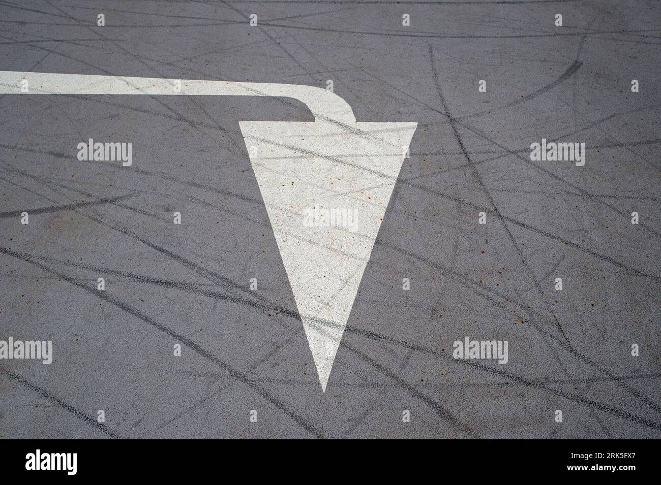 White painted arrow on a road surface, pointing down Stock Photo
