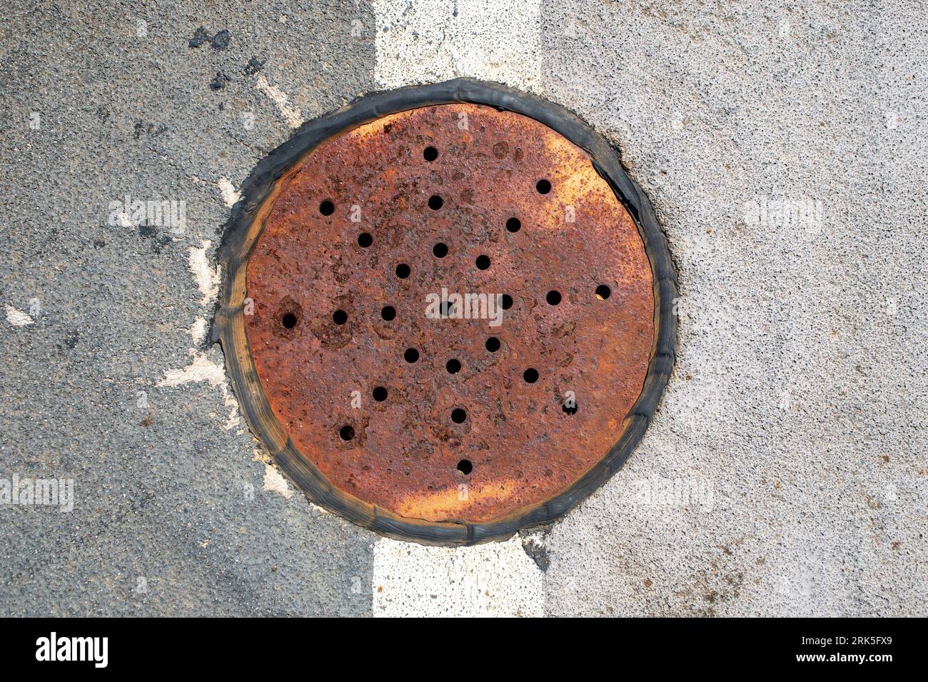 rusty drain cover in road surface, top down view. Stock Photo