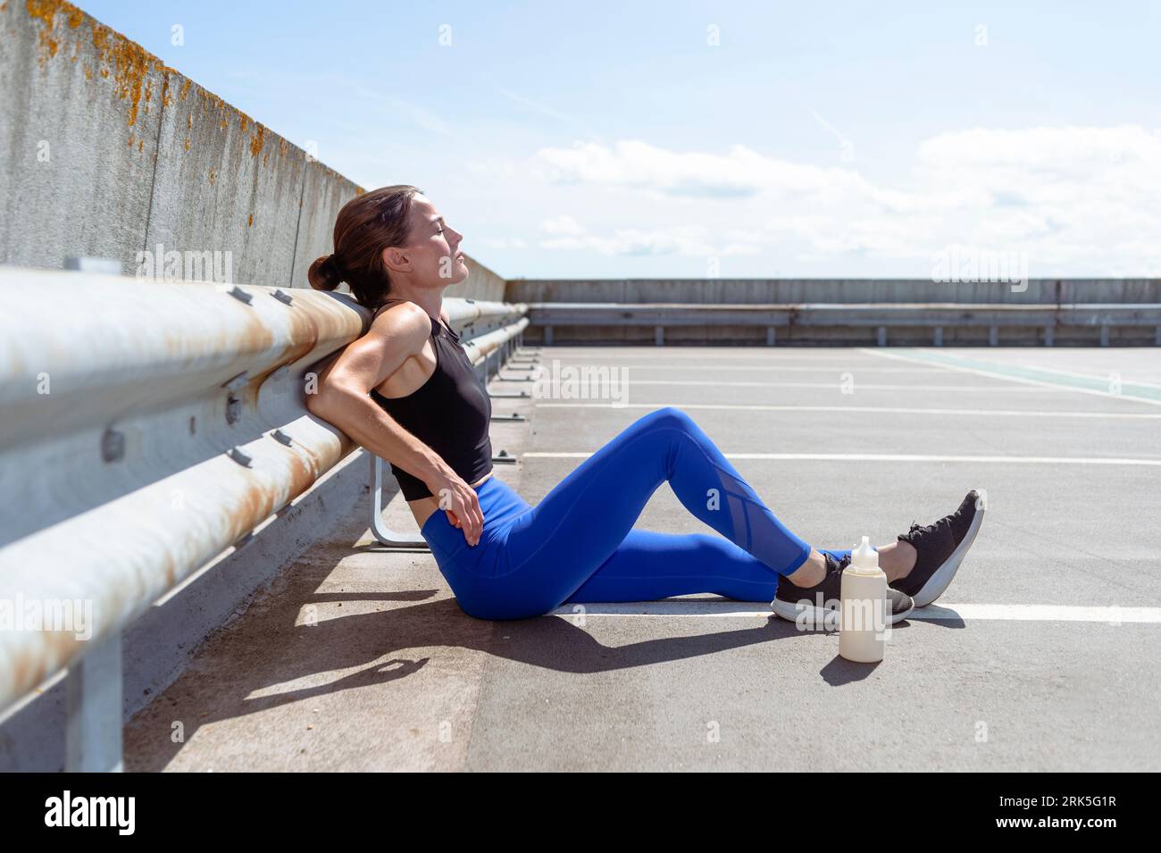 Exhausted female runner sitting on the floor after exercise outside in the sun Stock Photo