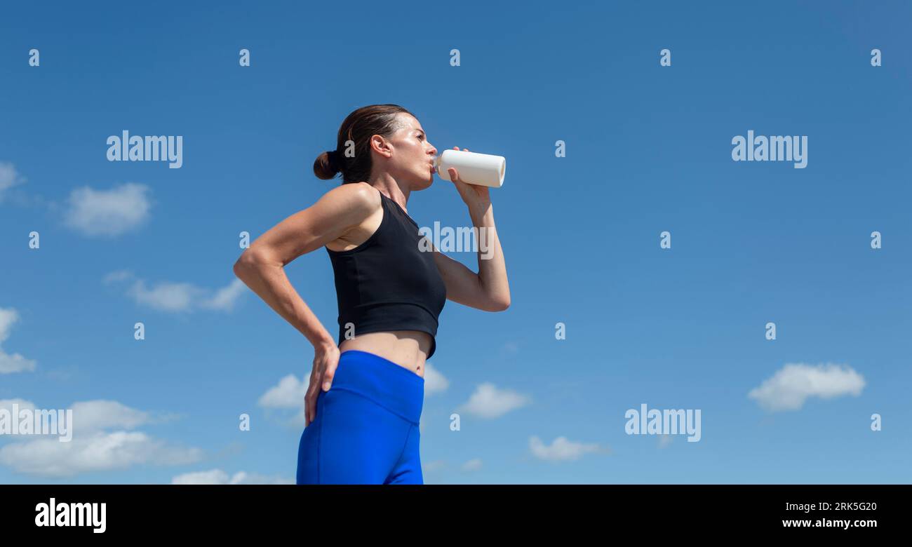 sportswoman drinking water from a glass bottle after exercising outside, blue sky background Stock Photo