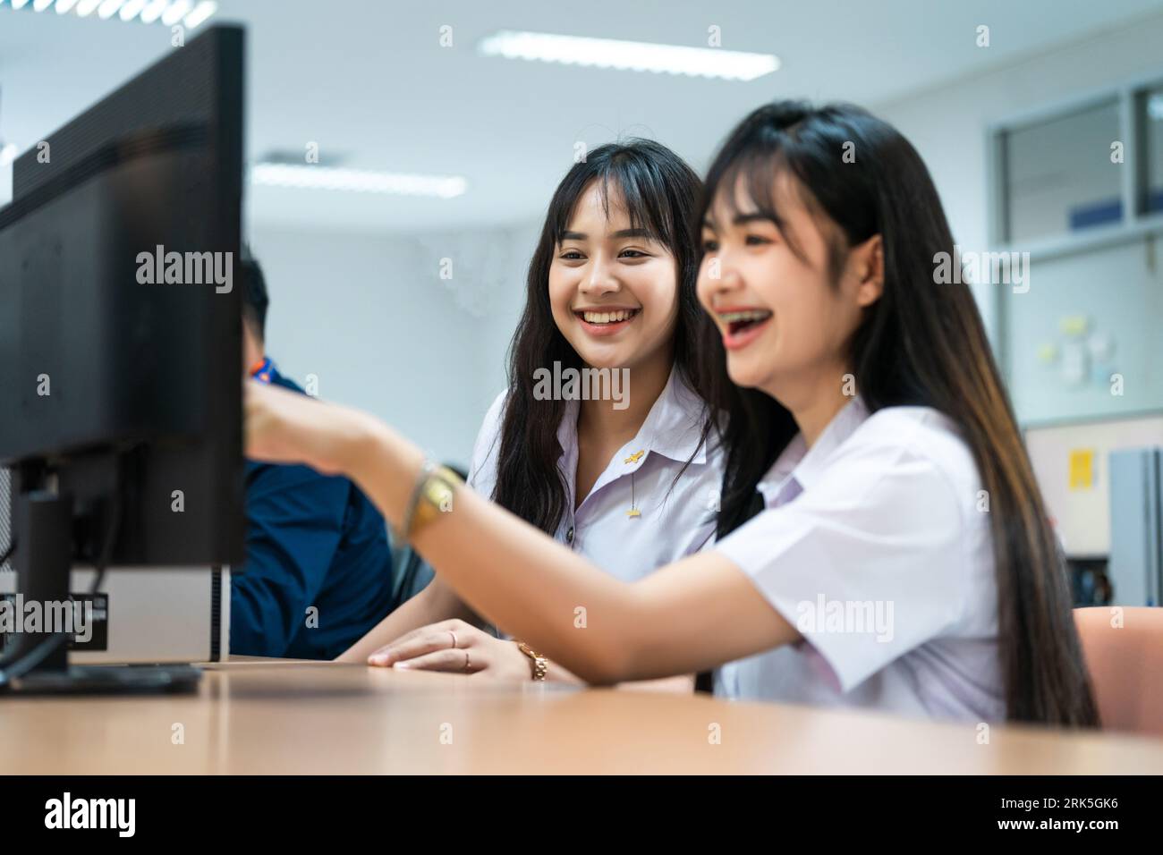 Two Asian female students smiling while pointing at a computer screen Stock Photo