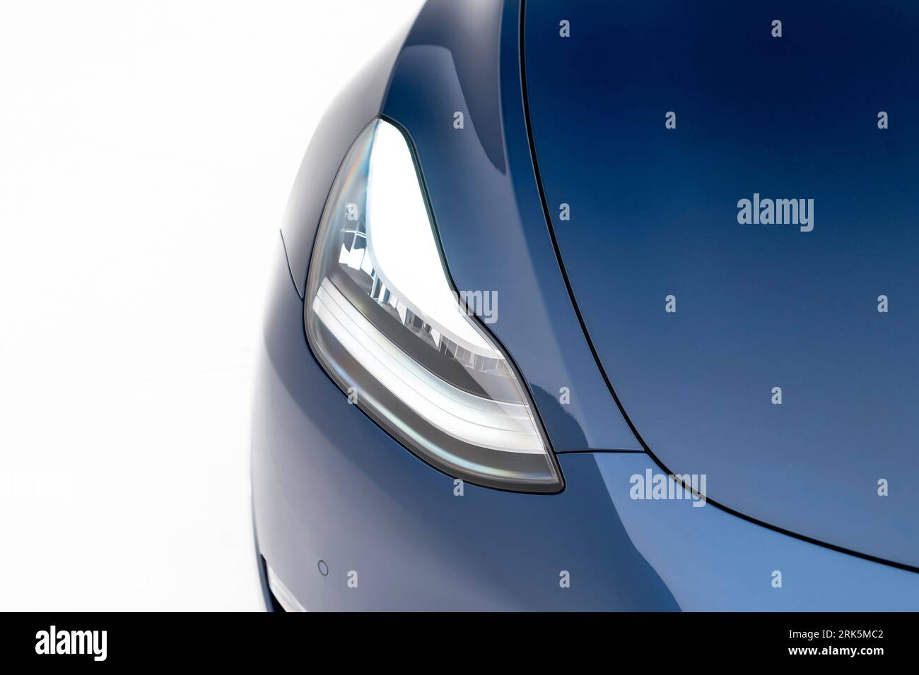 A blue Tesla with a front grille that is illuminated by bright white