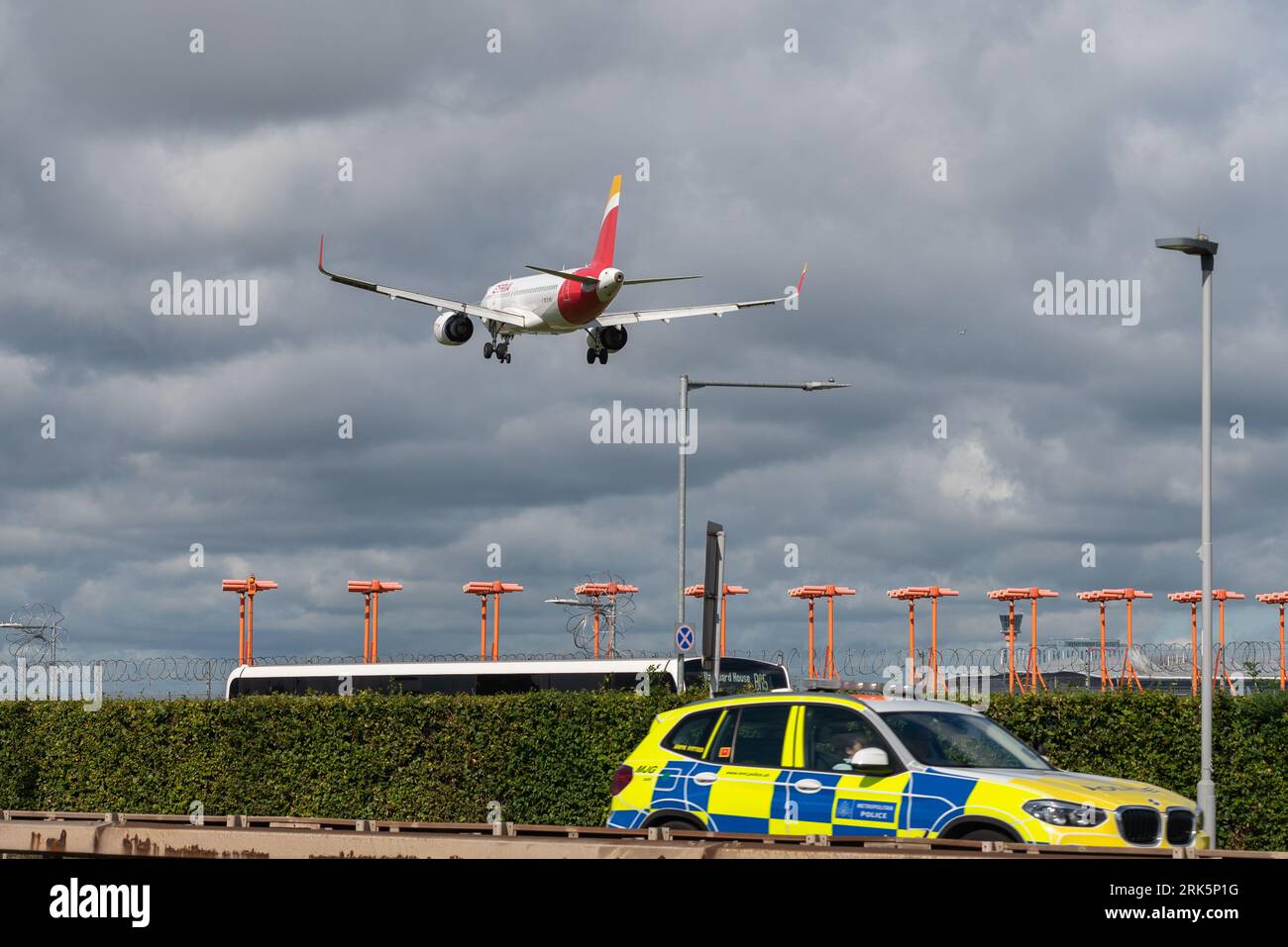 Police car driving on A30 road, passing runway threshold with jet