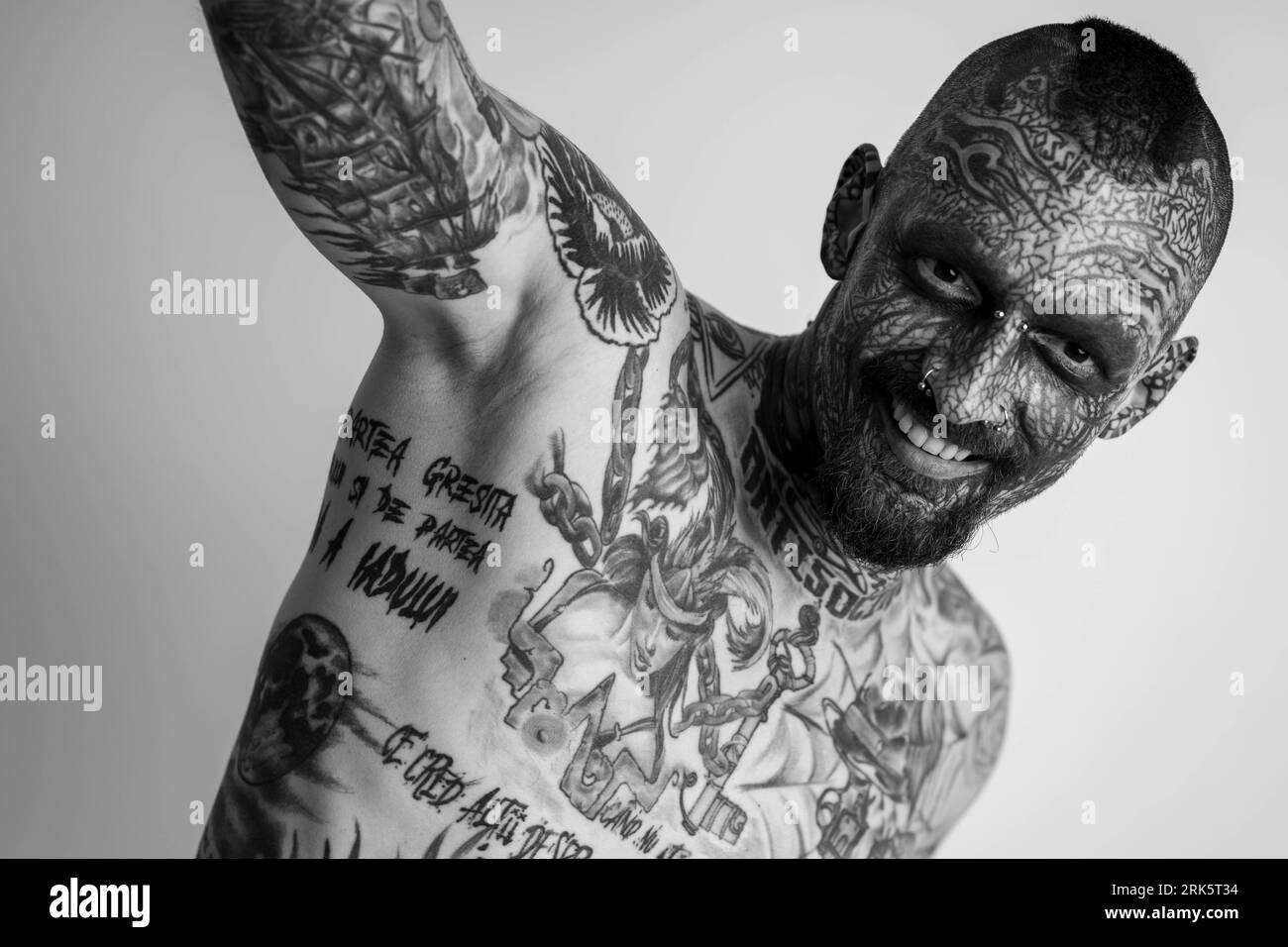 A portrait of a Caucasian man with full body coverage of traditional tattoos standing against a white background Stock Photo