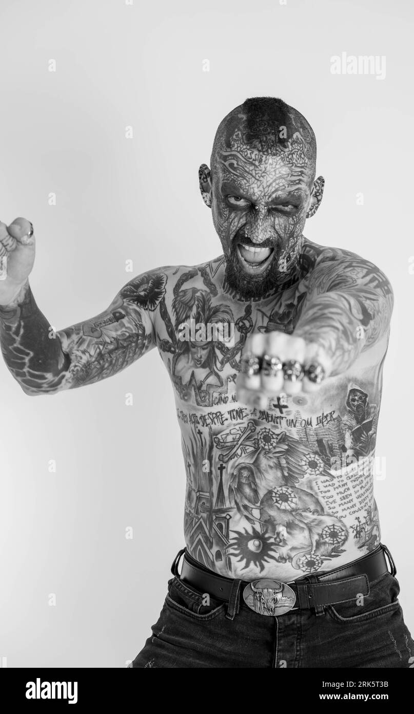 A black and white portrait of a Caucasian man with a full body of traditional tattoos against a white background Stock Photo