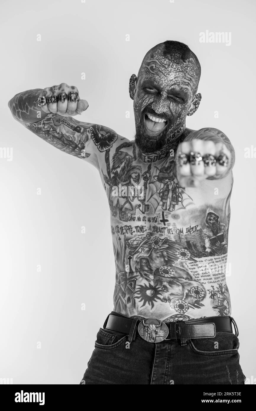 A grayscale portrait of a Caucasian man with a full body of traditional tattoos against a white background Stock Photo