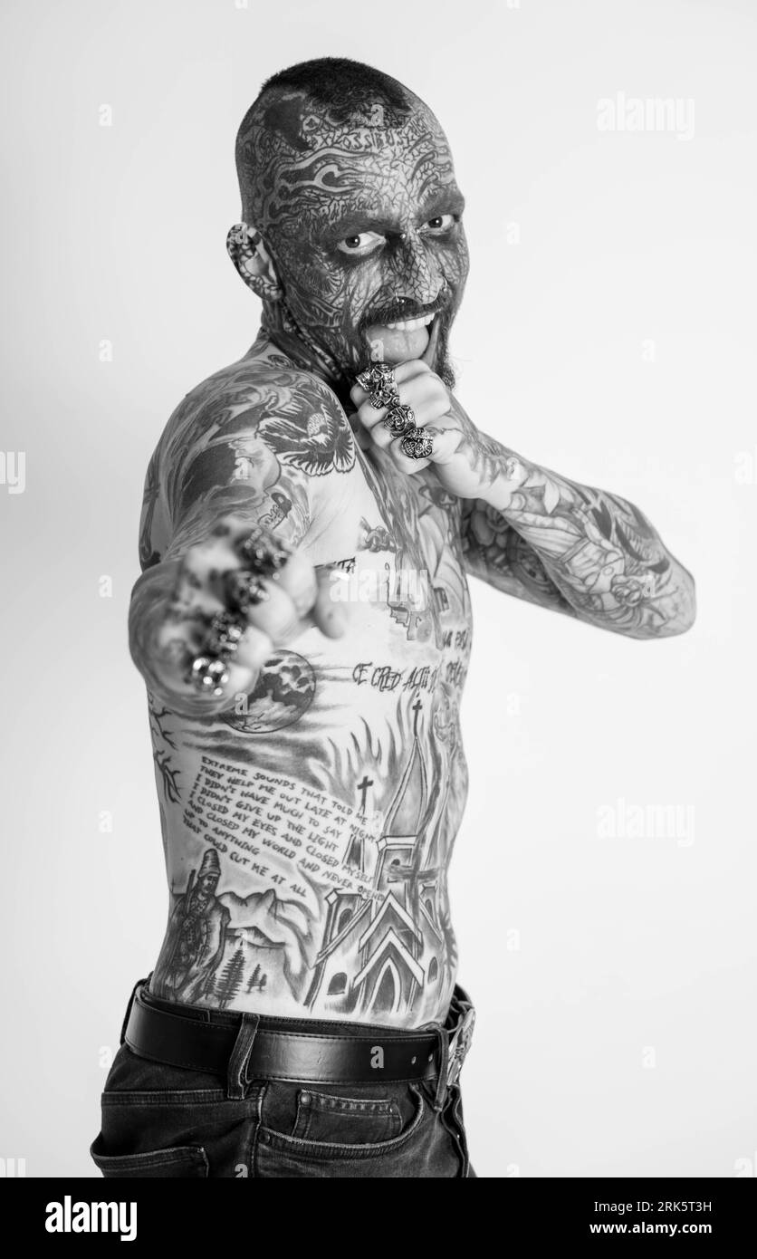 Grayscale portrait of a Caucasian man with full body traditional tattoos, set against a plain white background Stock Photo