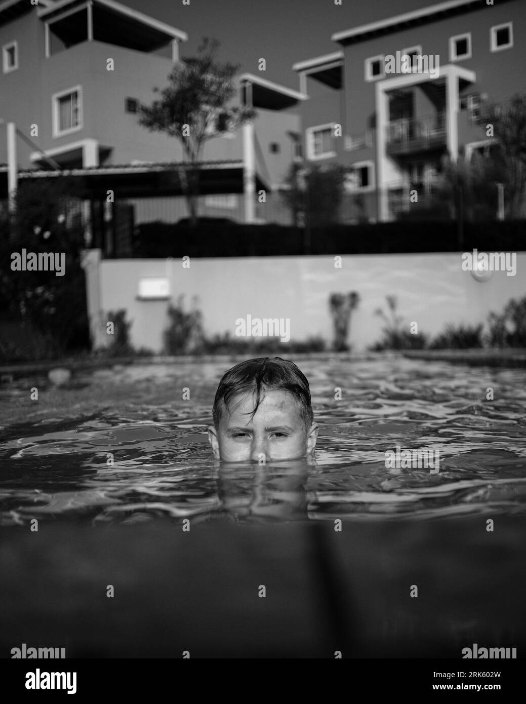 A young boy is submerged in a swimming pool, with his head tilted downwards, black and white image Stock Photo