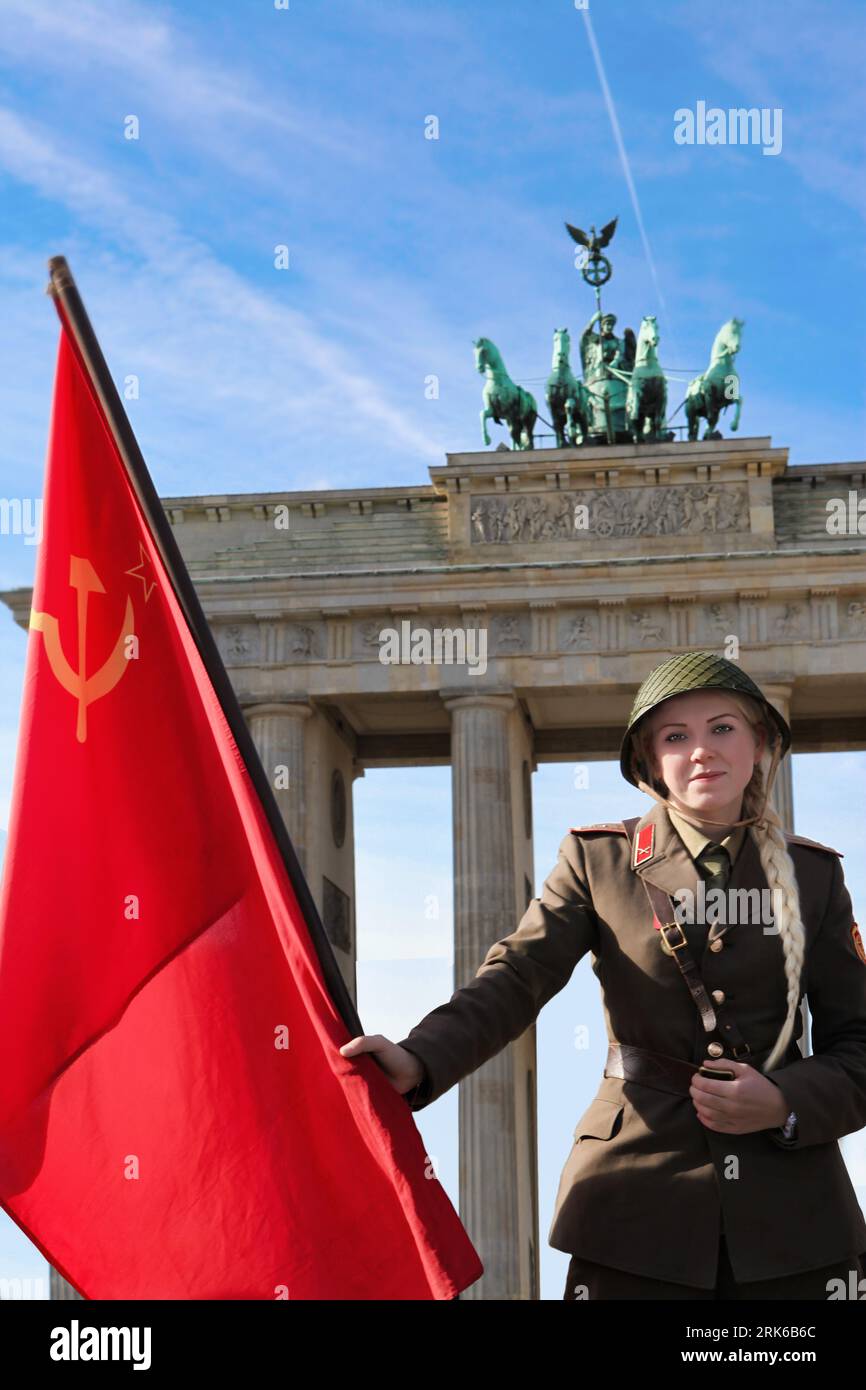 A female soldier standing in front of the Berlin Brandenburg Monument, holding a Soviet Union flag. Stock Photo