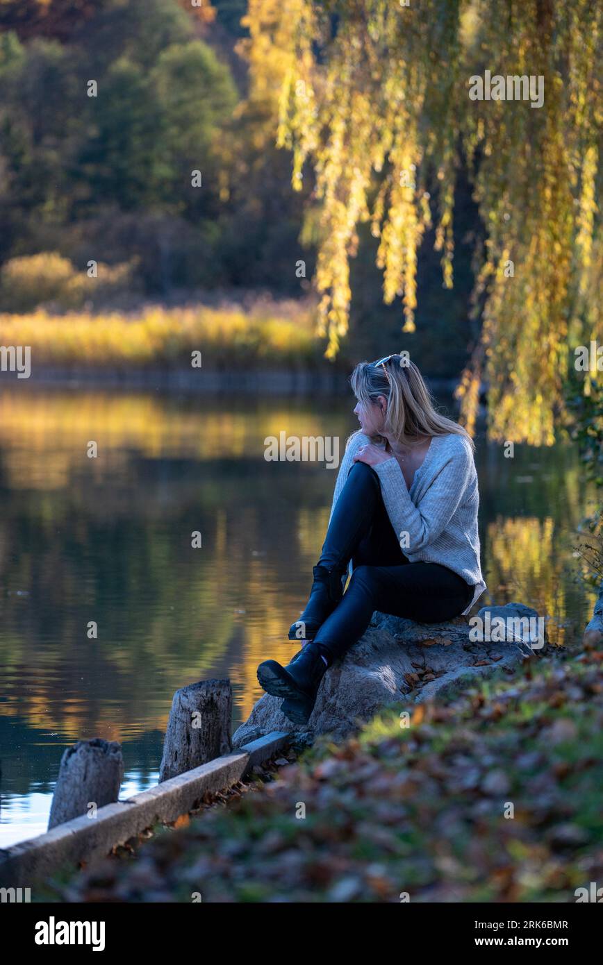 A young female perched on the edge of a riverbank, her face illuminated by a warm, glowing light. Stock Photo