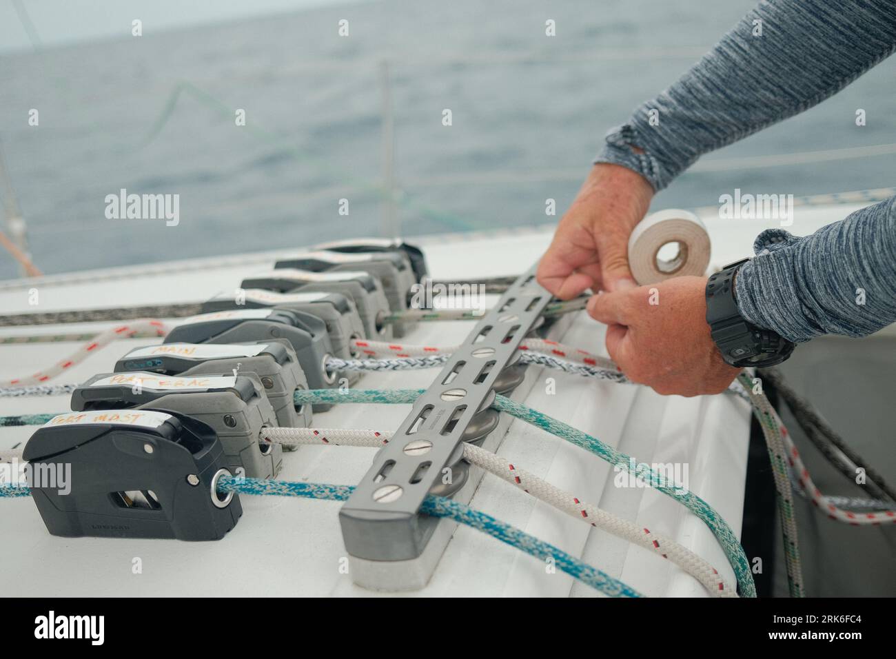 A person performing maintenance on a sailboat, tightening ropes and