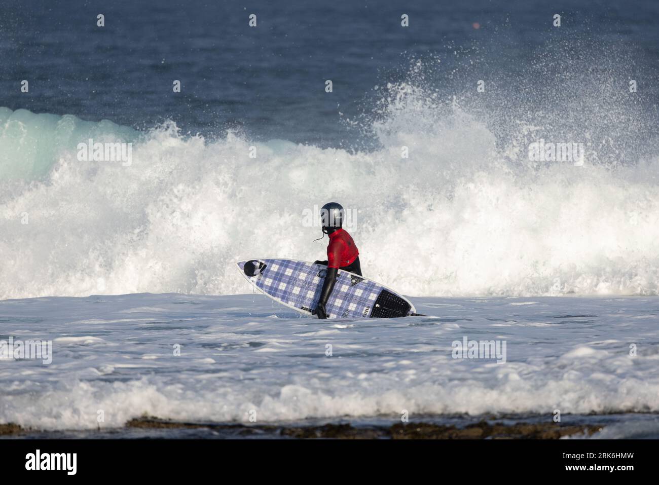 A male figure standing in the ocean waves, carrying a surfboard under