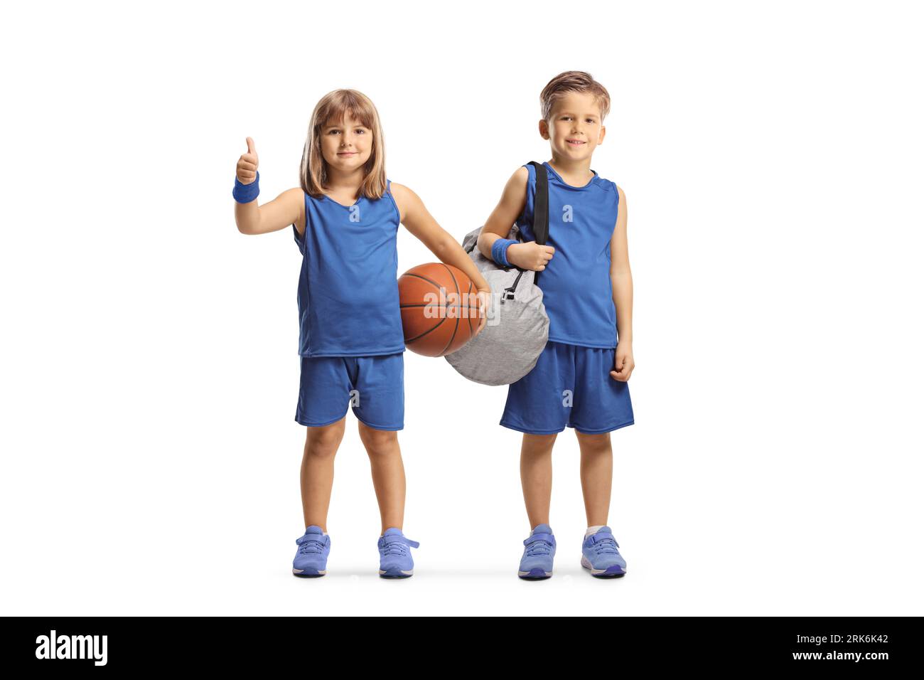 GIrl and boy in sport jerseys holding a basketball and gesturing thumbs up isolated on white background Stock Photo