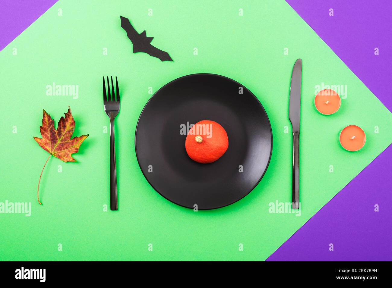 Halloween green and purple table place setting with decorative pumpkin, bat, autumn leaf and orange candles. Top view, flat lay. Stock Photo