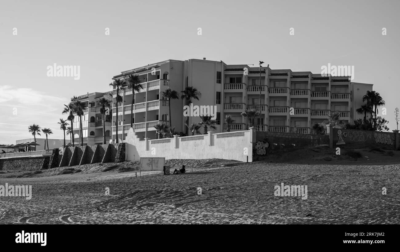 A tranquil scene of a building with an entrance in the foreground, situated beside a beach and surrounded by tall palm trees in the background Stock Photo