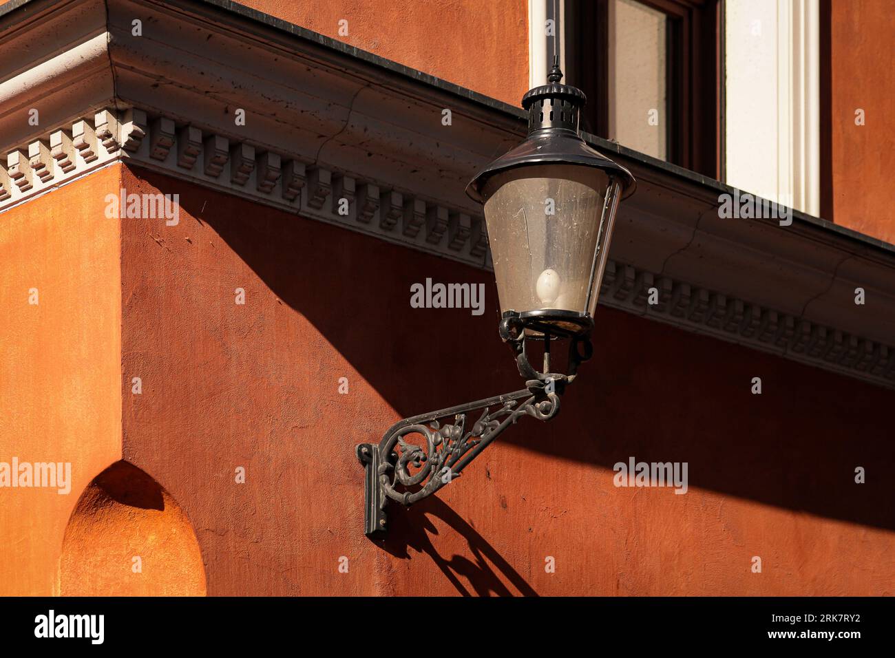 A vintage street lamp is affixed to the wall of an orange structure Stock Photo