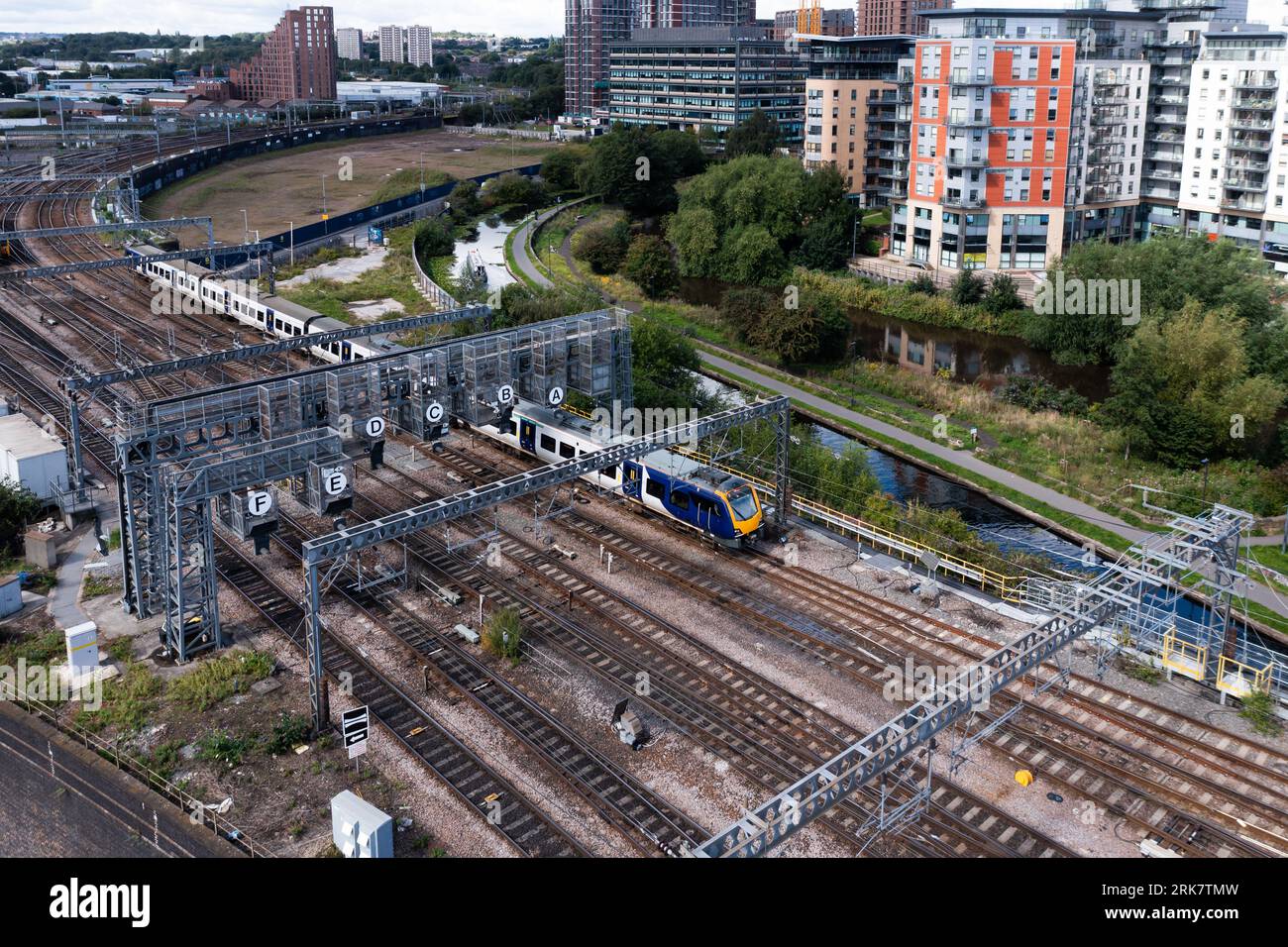 An aerial view of a passenger train travelling through a major rail junction with overhead gantry signals that have been annotated with letters to hel Stock Photo