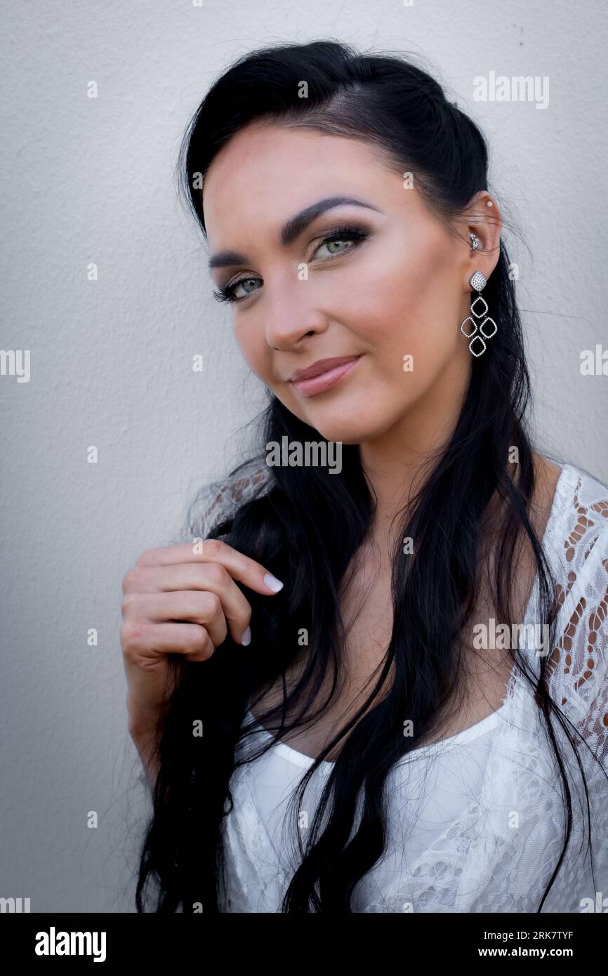 Gorgeous young woman with dark hair looking into the camera while styling her hair with one hand Stock Photo