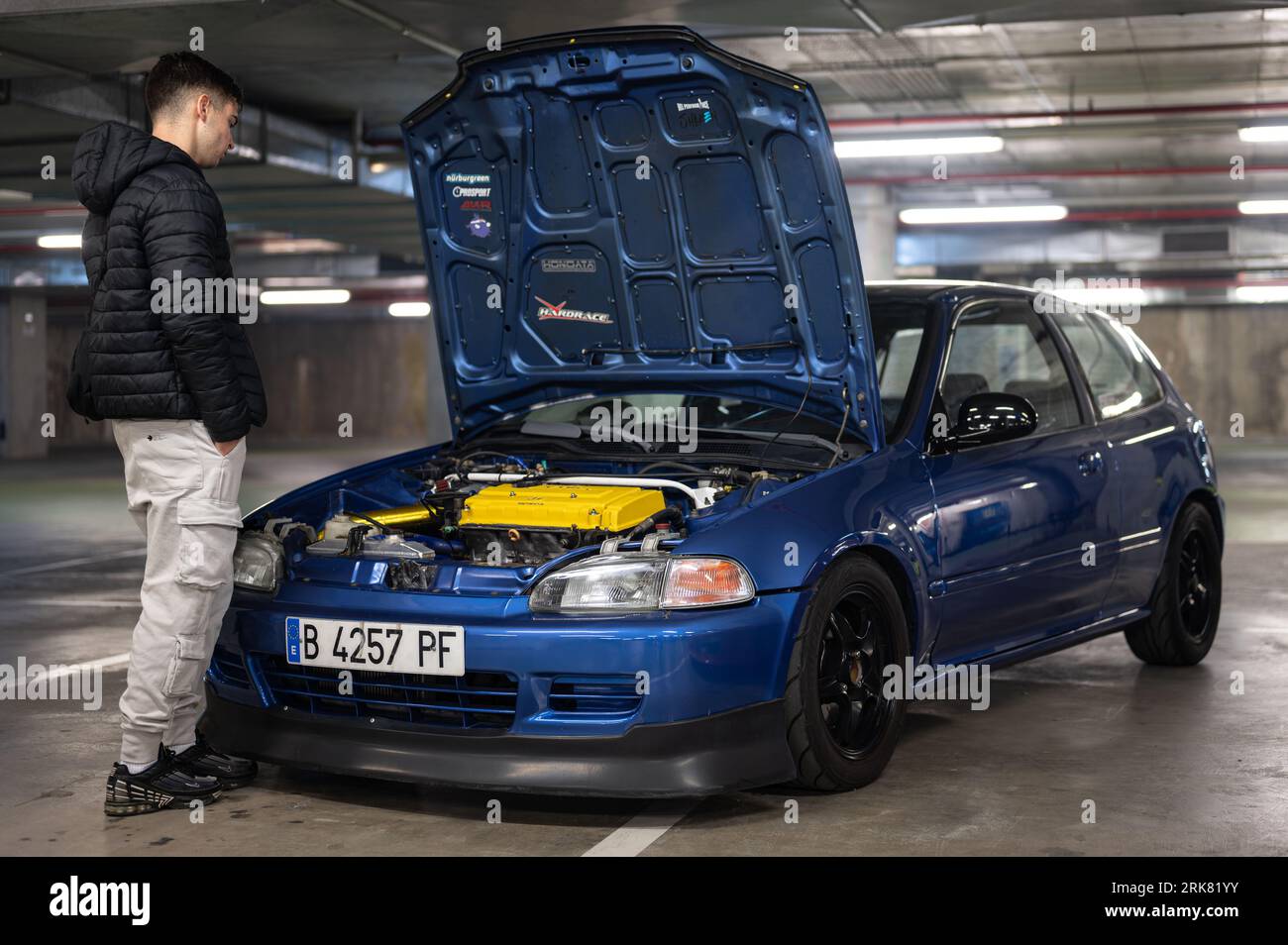 A young man looking at the engine of a Honda Civic EG 1.6 Vtec, the car is blue in color and the hood is open Stock Photo