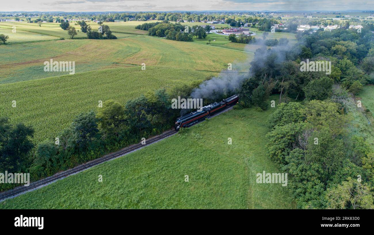 A train engine in an open area is emitting billowing clouds of smoke from its smokestack Stock Photo