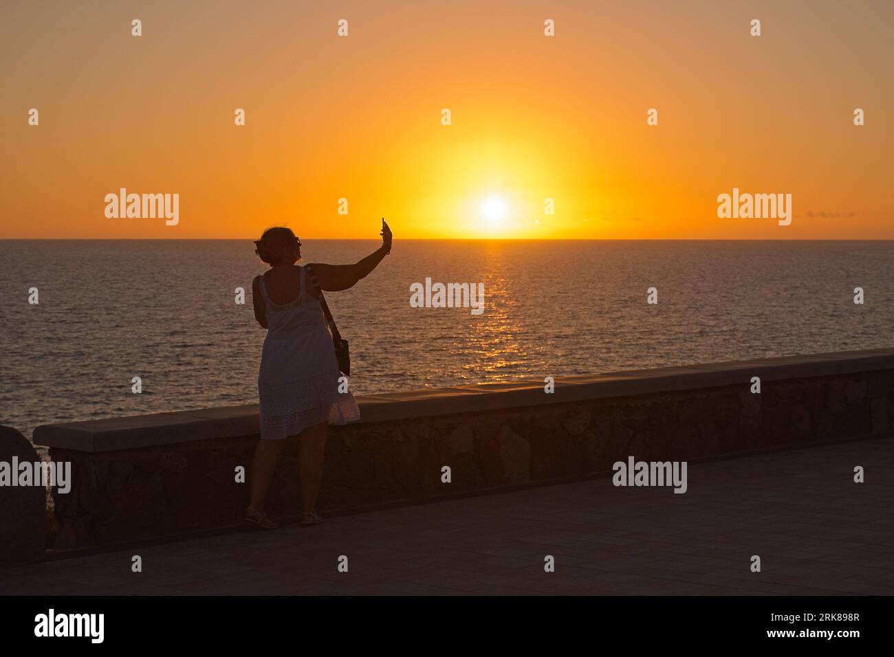 Silhouette of a woman taken herself a selfie against sun during sunset in Maspalomas, Gran Canaria, Spain Stock Photo